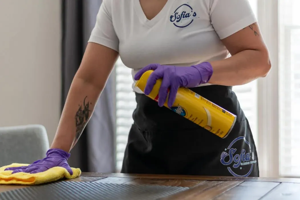 A cleaner spraying and wiping a dining table with a microfiber cloth