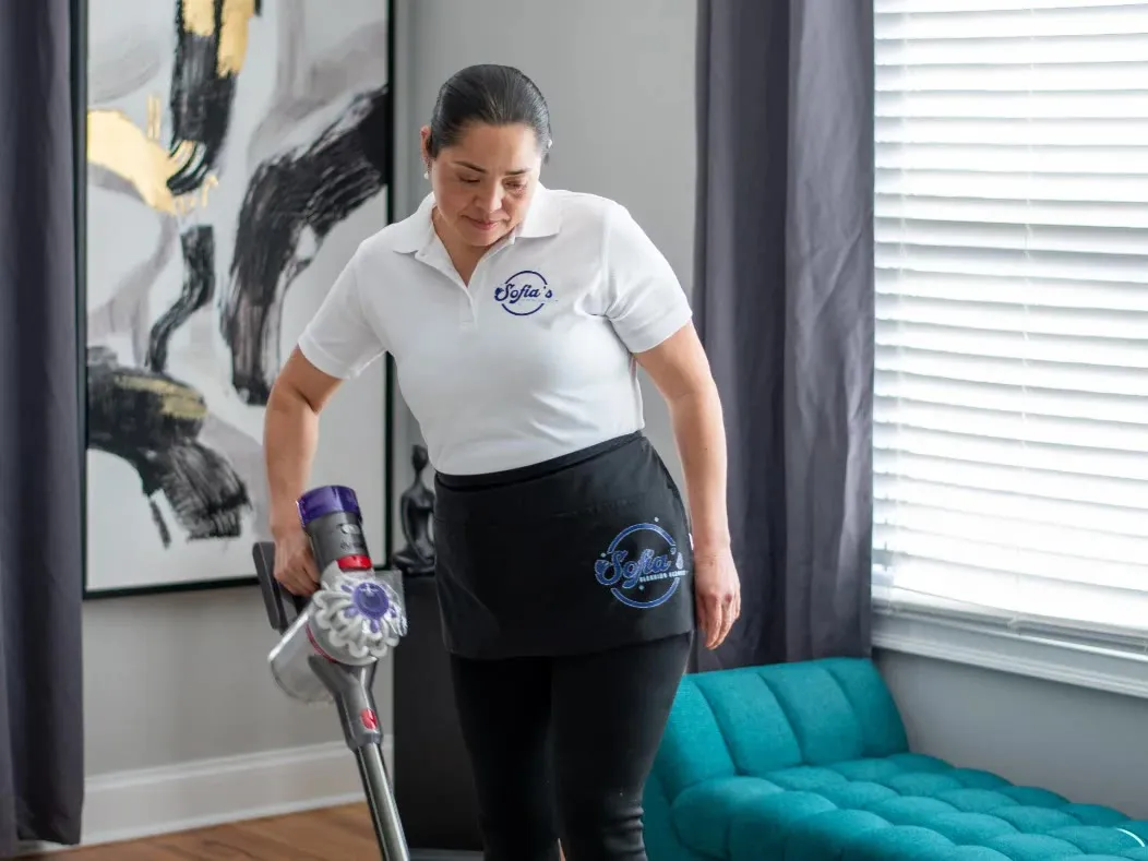 A cleaner vacuuming a rug beside a teal velvet sofa